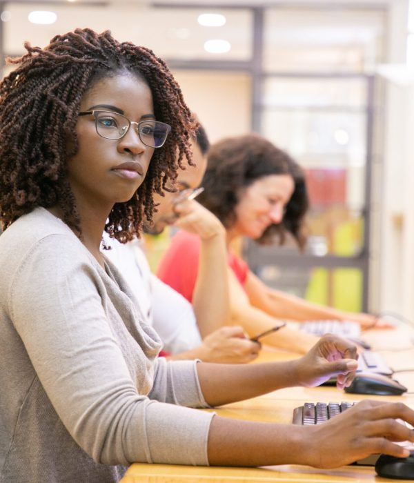 African American adult student working in computer class. Line of man and women in casual sitting at table, using desktops, typing. Staff training concept
