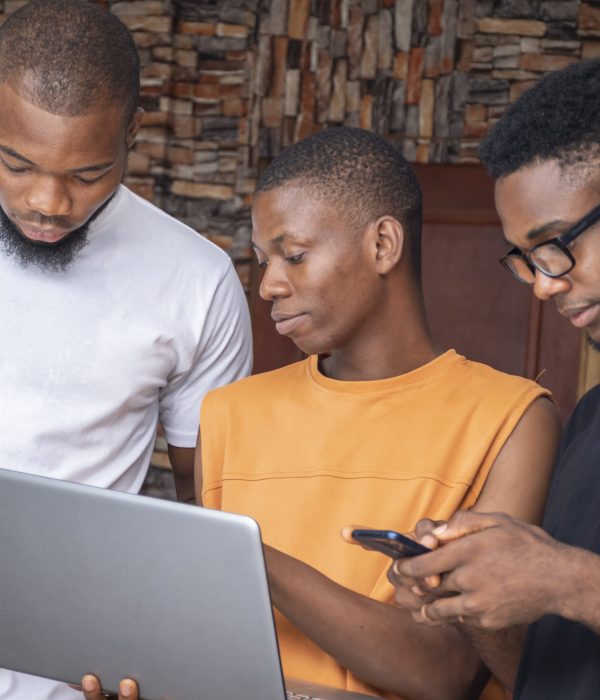 A group of young African males discussing a project while using their laptop and phones